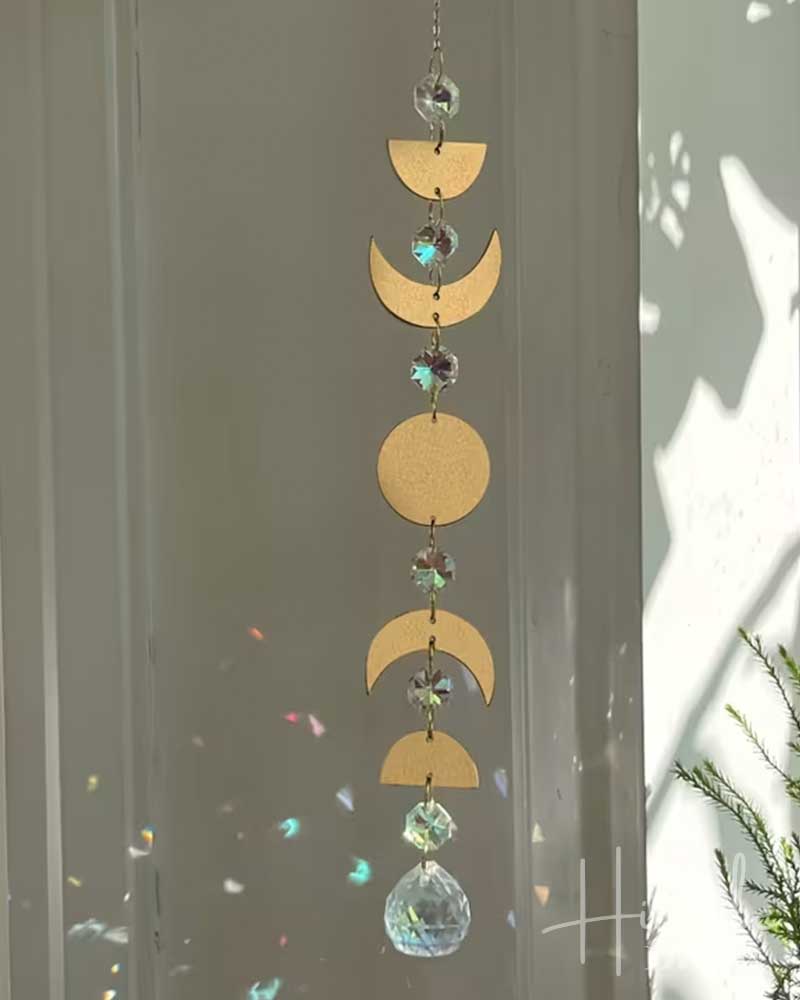 Decorative hanging with gold moon phases and crystal elements against a neutral background