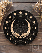 Decorative pendulum board with moon phases and lotus flower design on a wooden surface with dried flowers.