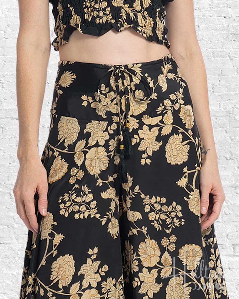 Person wearing a black and gold floral outfit against a white brick wall.