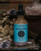 A bottle of Intuitive Witch Sacred Spell Water with a turquoise label and black dropper cap, styled on a rustic wooden surface with crystals and dried botanicals.