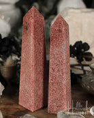Two Raspberry Aventurine crystal obelisks on a wooden surface with blurred background