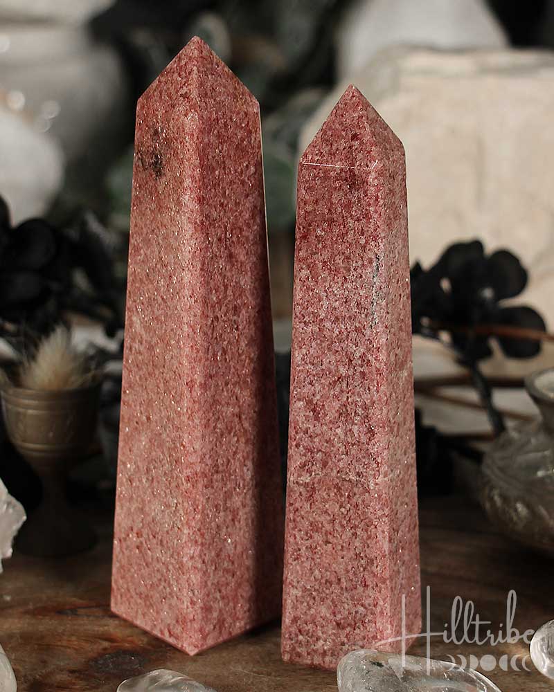 Two Raspberry Aventurine crystal obelisks on a wooden surface with blurred background