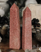 Two Raspberry Aventurine crystal obelisks on a wooden surface with blurred background