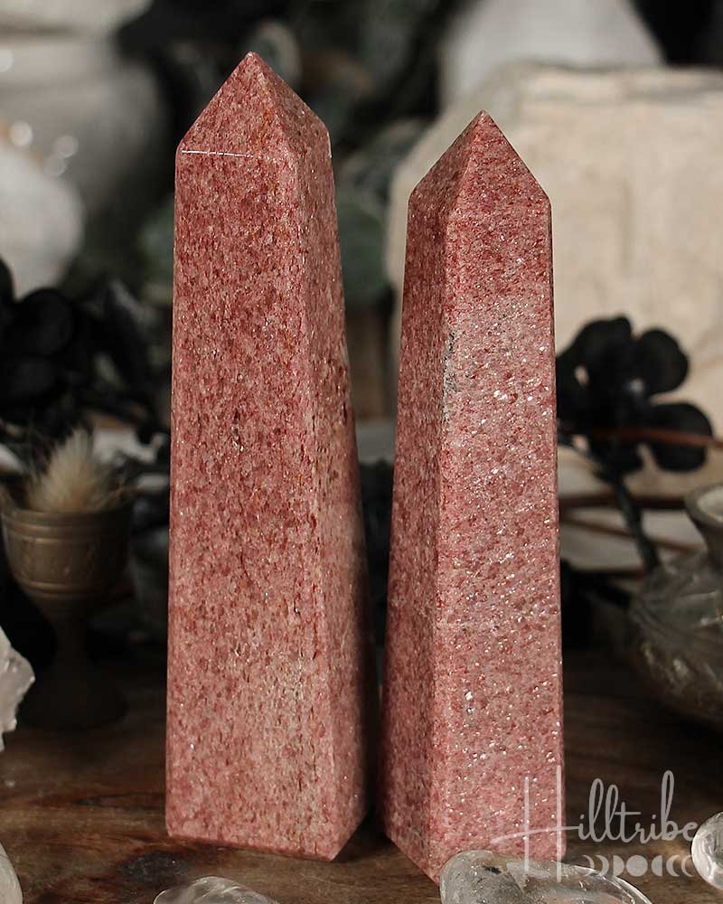 Two Raspberry Aventurine crystal obelisks on a wooden surface with blurred background
