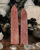 Two Raspberry Aventurine crystal obelisks on a wooden surface with blurred background
