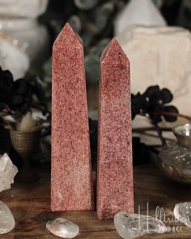 Two Raspberry Aventurine crystal obelisks on a wooden surface with blurred background