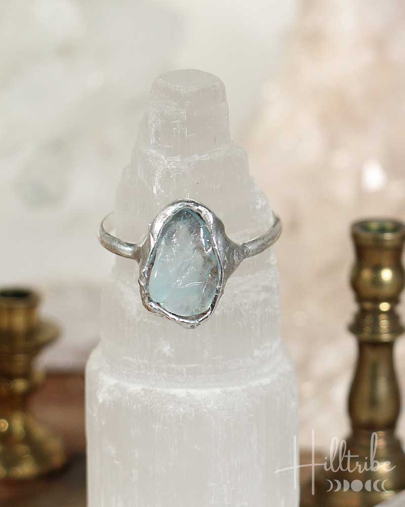 Silver ring with a large, rough-cut gemstone on a white pedestal with a blurred background