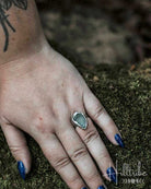 Hand wearing a ring with a stone on a mossy background