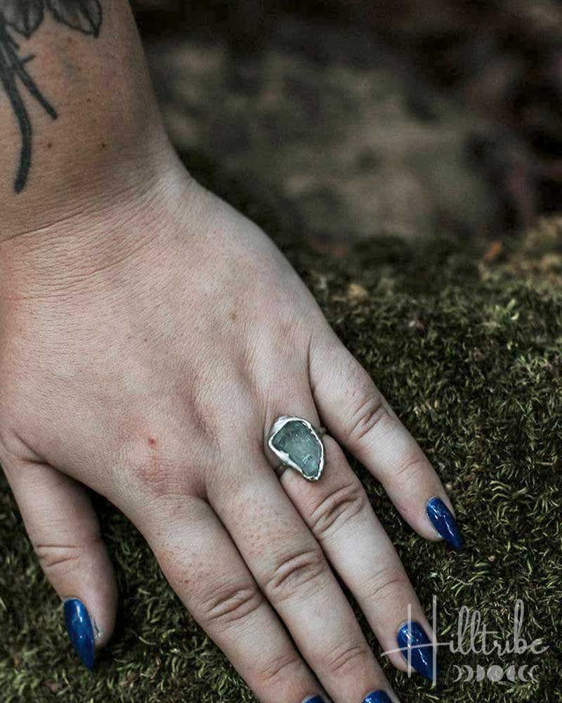 Hand wearing a ring with a stone on a mossy background