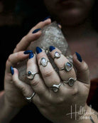 Close-up of hands with multiple rings and blue nail polish holding a crystal, with 'Hilltribe' branding.
