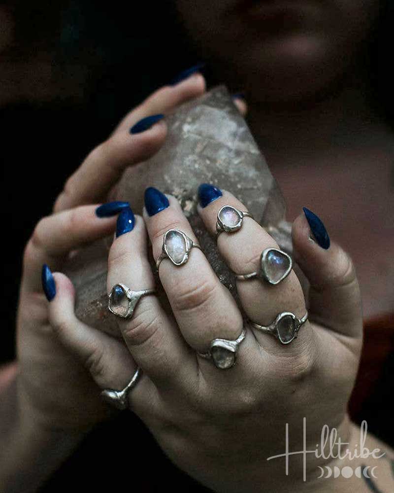 Close-up of hands with multiple rings and blue nail polish holding a crystal, with 'Hilltribe' branding.