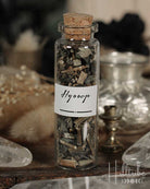 Glass bottle with cork lid containing herbs labeled 'Hyssop' on a wooden surface.
