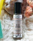 A 10ml bottle of Road Opener Lemongrass Stimule QUADE crystal infused blend oil, featuring a black cap and white label with black text, styled on a white faux fur surface with crystals and dried flowers.