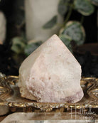 Rose Pink Amethyst Cut Base crystal on a decorative stand with blurred greenery in the background