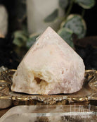 Rose Pink Amethyst Cut Base crystal on a decorative stand with blurred greenery in the background