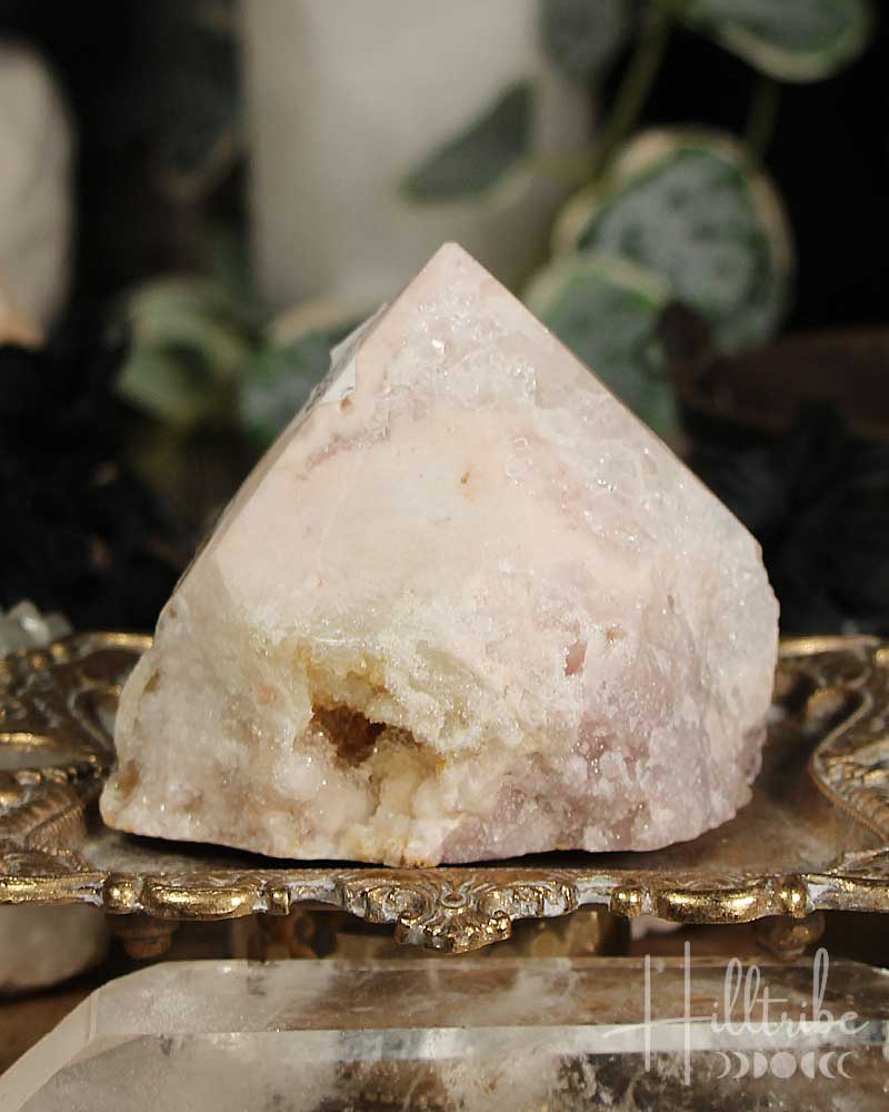 Rose Pink Amethyst Cut Base crystal on a decorative stand with blurred greenery in the background