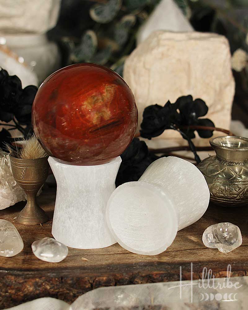 Decorative setting with a red sphere on a white stand, surrounded by crystals and black flowers.