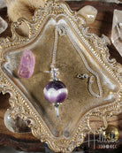 Sephoroton Amethyst Pendulum on an ornate gold display stand with crystals in the background.