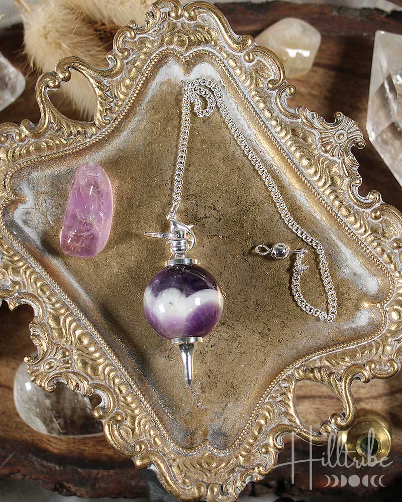 Sephoroton Amethyst Pendulum on an ornate gold display stand with crystals in the background.