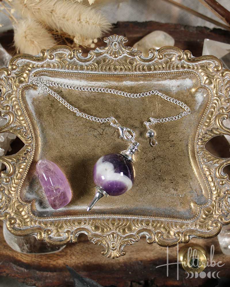 Sephoroton Amethyst Pendulum on an ornate gold display stand with crystals in the background.