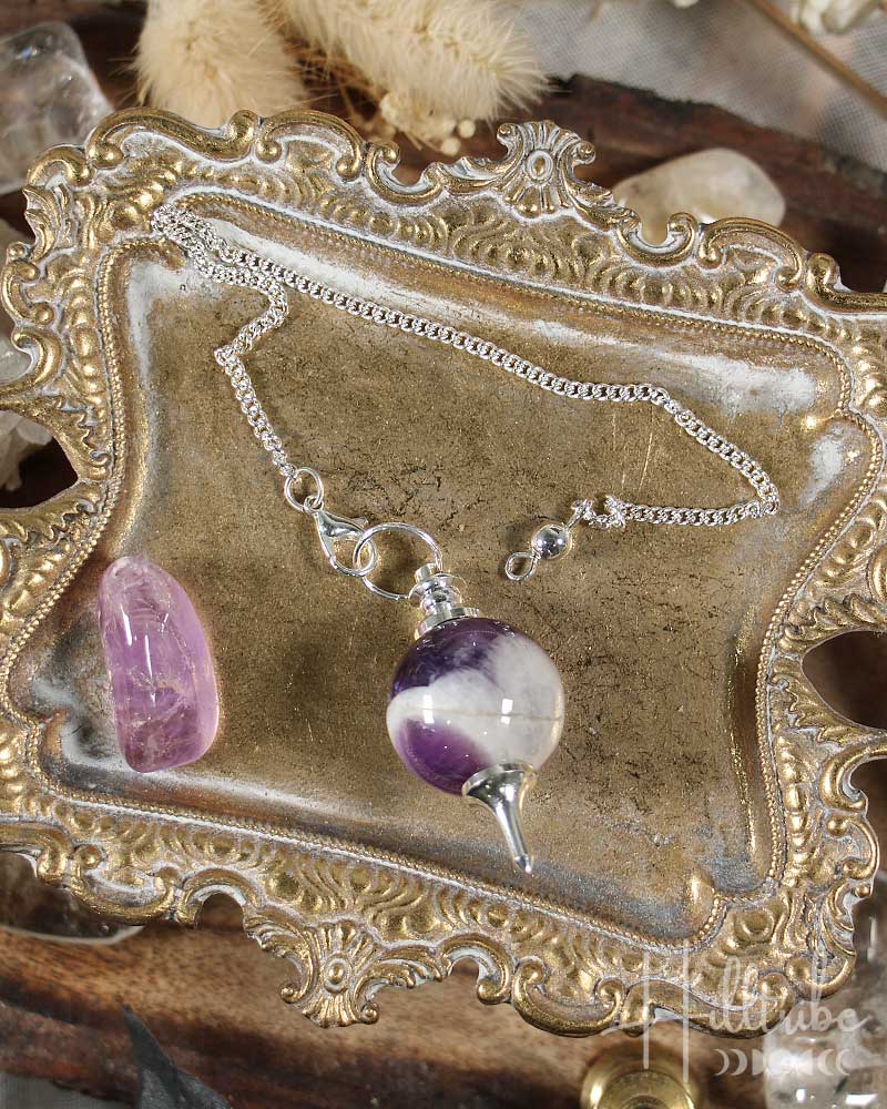 Sephoroton Amethyst Pendulum on an ornate gold display stand with crystals in the background.