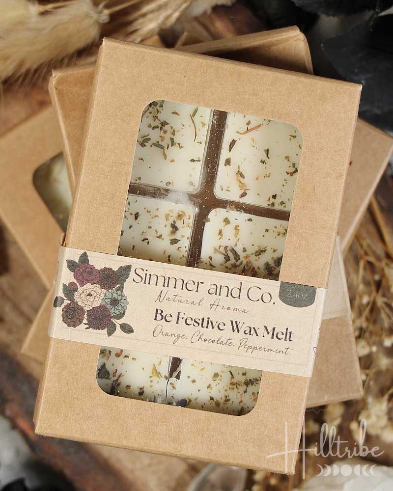Festive wax melt packaging with cinnamon sticks, orange slices, and dried leaves on a wooden surface.