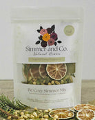 A stand-up pouch of Simmer and Co. 'Be Cozy Simmer Mix' natural home fragrance, featuring dried citrus slices, cardamom pods, and botanicals visible through a clear window, with dried citrus slices and rosemary styled in the foreground.