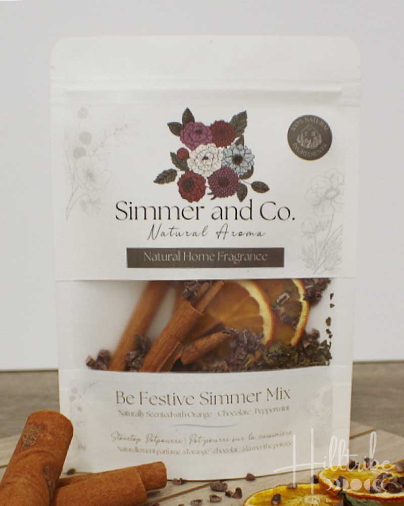 A white stand-up pouch of Simmer and Co. 'Be Festive Simmer Mix' natural home fragrance, shown on a light background with cinnamon sticks and dried citrus slices around it.