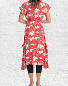 Red floral dress worn by a person against a white brick wall.