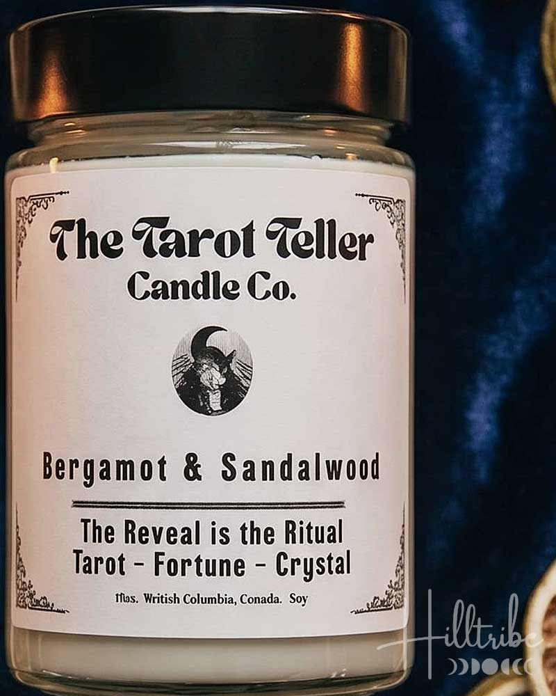 A jar candle labeled 'The Tarot Teller Candle Co.' in the scent Bergamot & Sandalwood, styled in a flat lay with dried orange slices, sandalwood pieces, a pocket watch, and tarot cards on a dark blue velvet background.