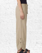Beige wide-leg pants with buttons on a white brick wall background
