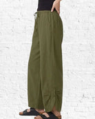 Person wearing olive green wide-leg pants against a white brick wall.