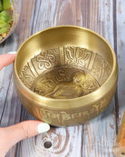 Brass singing bowl with intricate designs held by a hand on a wooden surface