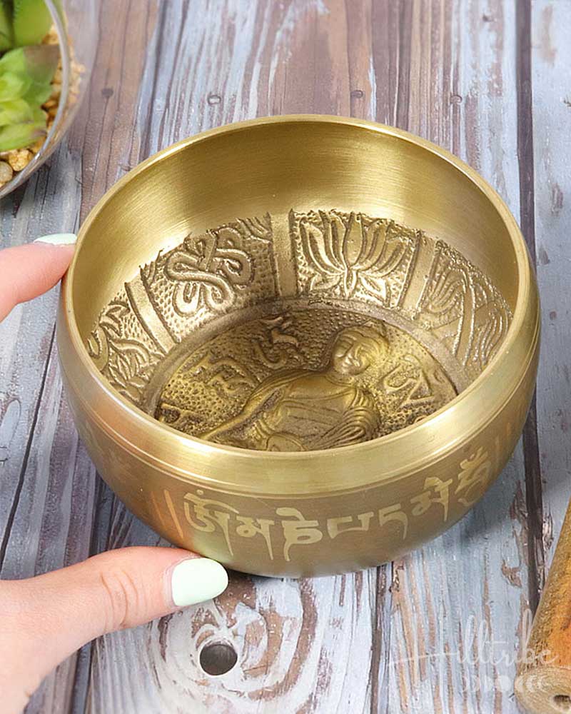 Brass singing bowl with intricate designs held by a hand on a wooden surface