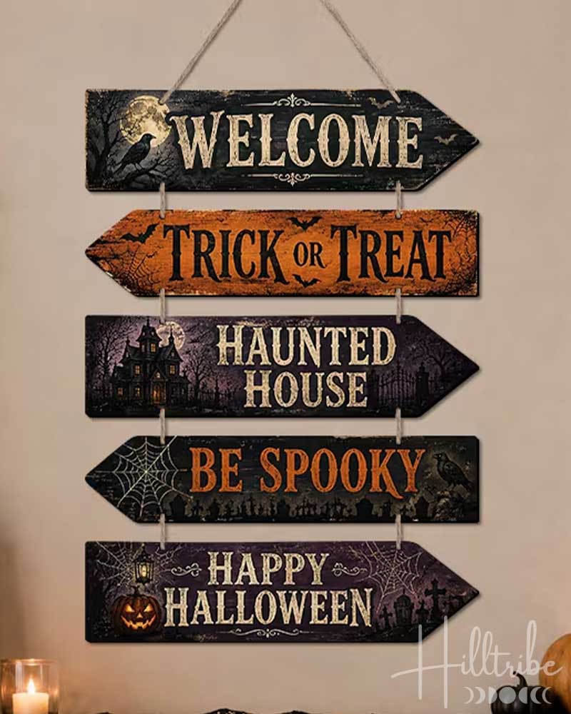 A 5-piece wooden arrow sign set for Halloween, hanging on a beige wall above a decorated mantel with pumpkins and candles. The sign features rustic distressed wood textures in black, orange, and purple, with cream lettering reading 'WELCOME', 'TRICK OR TREAT', 'HAUNTED HOUSE', 'BE SPOOKY', and 'HAPPY HALLOWEEN'.