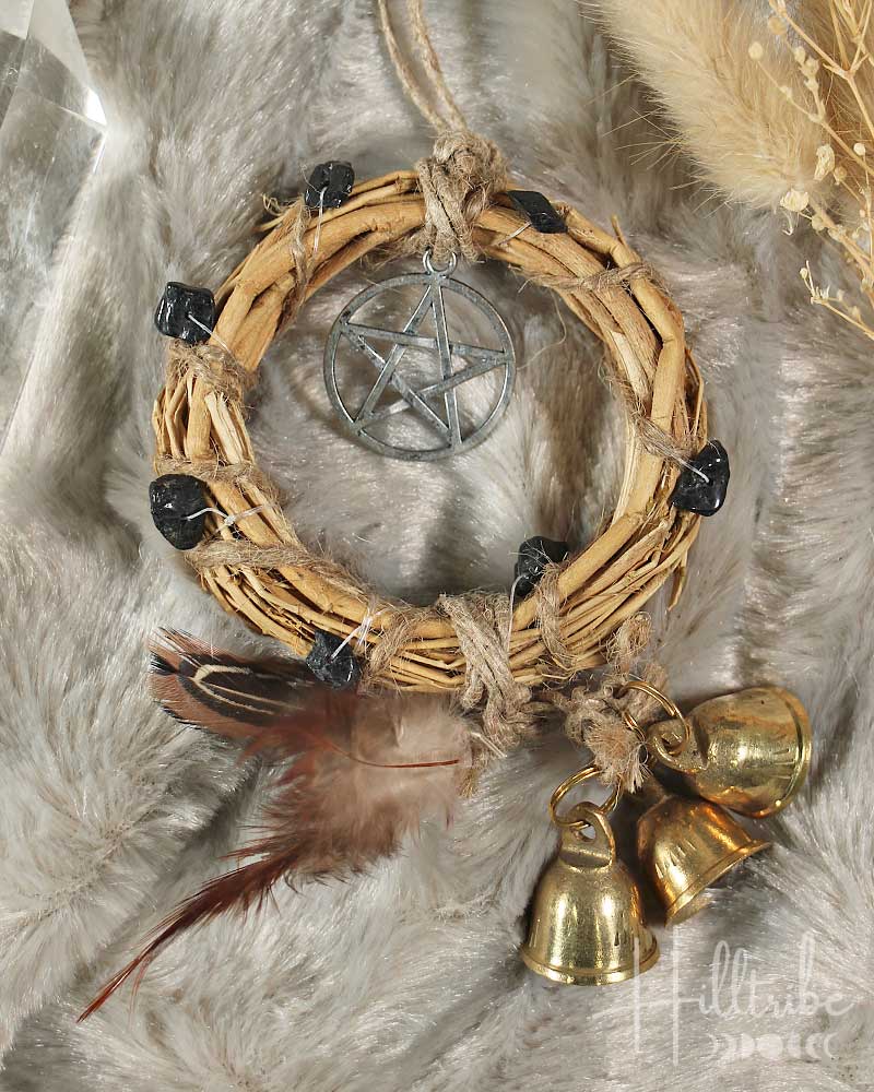 Woven wreath with pentacle pendant, feathers, and gold bells on a fur background