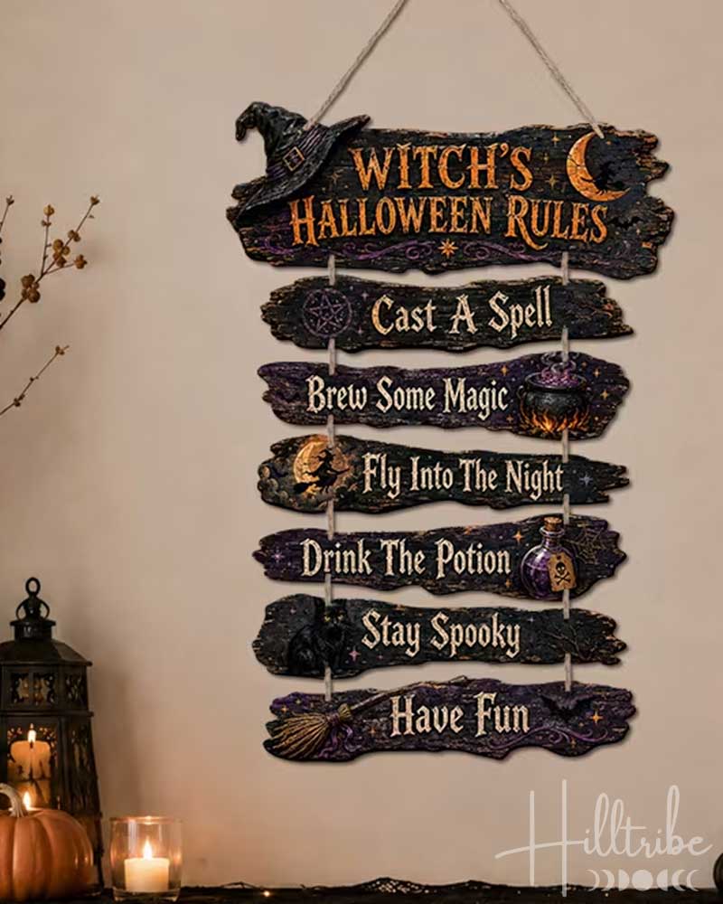 A rustic multi-tier wooden hanging sign with Halloween-themed text, displayed on a wall above a decorated table with pumpkins, candles, and dried branches. The sign reads: 'Witch's Halloween Rules' with additional phrases below.